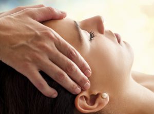 Close up head portrait of young woman having facial massage in spa. Therapist massaging womans head against colorful background.